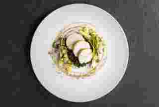 Succulent sliced chicken atop a bed of lentils, garnished with herbs and drizzled with a rich sauce, beautifully presented.