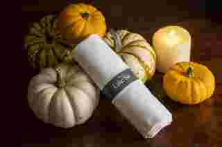 White napkin with The Lake Isle label among decorative pumpkins and a lit candle on a wooden table.