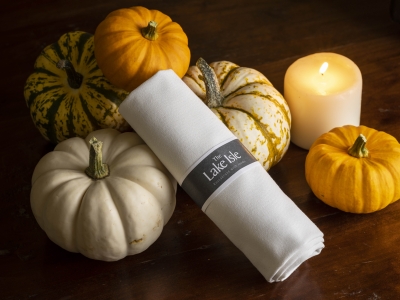 White napkin with The Lake Isle label among decorative pumpkins and a lit candle on a wooden table.